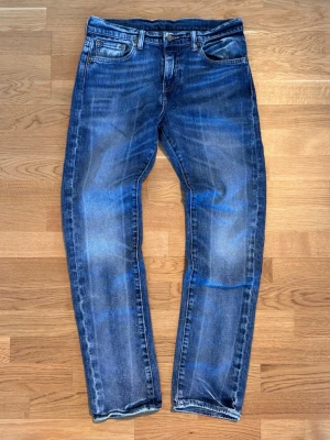 Levi's blå jeans med slitningar - Säljer ett par klassiska blå Levi's jeans med snygga slitningar och tvättade detaljer. Jeansen har fem fickor, raka ben och en läderpatch bak i midjan. Materialet är robust denim som ger en cool och avslappnad look. Pris går att diskuteras om du har frågar är de bara att skriva ett meddelande till mig 