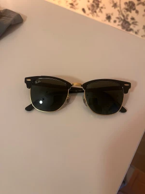 Svarta Ray ban solglasögon  - Snygga solglasögon med svart rektangulär båge och tunna skalmar. Glasögonen har guldfärgade detaljer vid näsbygeln och gångjärnen för en extra stilren look. Perfekta för dig som vill ha en klassisk men trendig accessoar.