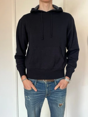 Mörkblå  hoodie med ficka framtill - En stilren svart hoodie med huva och dragsnören. Hoodien har en stor känguruficka framtill och ribbade muddar vid ärmslut och nederkant. Perfekt för en avslappnad look och enkel att matcha med jeans eller joggers.