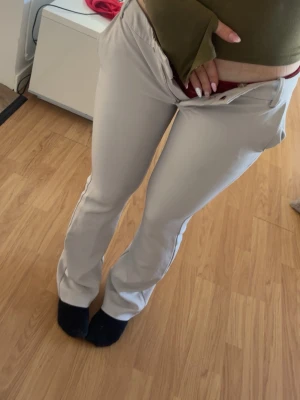 Beiga utsvängda kostymbyxor - Snygga beiga kostymbyxor med utsvängda ben och klassisk passform. Byxorna har hällor för skärp, två bakfickor och stängs med knapp och dragkedja. Perfekta för en stilren look och lätta att matcha med olika toppar.