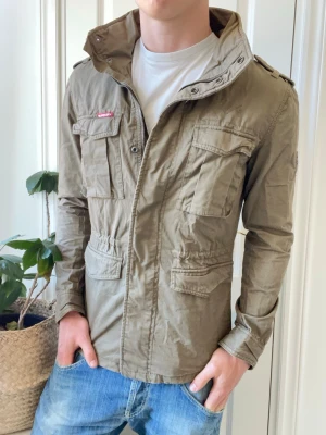 Superdry fieldjacket  - Superdry fieldjacket - första bilden är på en jacka som är Strolek S. Det är så den ska sitta, då den jackan som säljs i denna annonsen är storlek L, som ni ser. Inga defekter! Modellen i bilderna är 180 cm 75 kg och bär Storlek L  , Kom med frågor! 🌟 (Kan gå ned i pris vid köp av paket 😉) 