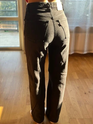 Levi’s jeans - Säljer ett par svarta jeans med rak passform och hög midja. Jeansen har klassiska fem fickor, knappgylf och är tillverkade i ett stadigt denimtyg. Perfekta för en clean och stilren look. Allt i dm