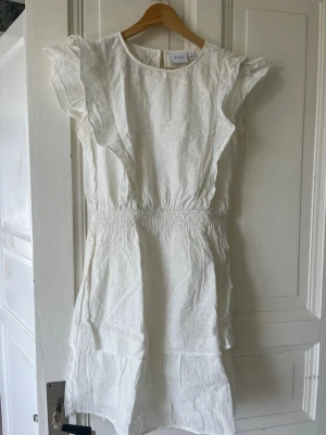 Vit klänning från Vila - Vit klänning från Vila med volanger och broderade detaljer. Perfekt till sommaren!🩷 Storlek 38 men lite liten i storleken. Bara att skriva för fler bilder🩷😇Klänningen är endast använd två gånger, så den är i bra skick.