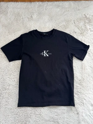 Svart t-shirt - Snygg svart t-shirt med klassisk logga i vitt på bröstet. T-shirten har rund hals och korta ärmar, tillverkad i mjuk bomull för en skön känsla. Perfekt basplagg med stilren design.