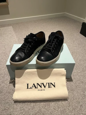 Svarta Lanvin sneakers i läder - Snygga blåa sneakers från Lanvin i äkta mocka med vita sulor och klassisk låg profil. Skorna har blåa skosnören och diskret design som passar till det mesta. Kommer med originalpåse och box från Lanvin Paris.