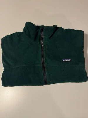 Patagonia full-zip fleecejacka, mörkgrön, XXL, herr - Patagonia full-zip i mjuk mikrofleece, djup skogsgrönt. Ståkrage, två handfickor, avslappnad herrpassform. Stl XXL herr. Skicka mig gärna era erbjudanden