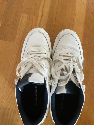 Vita Björn Borg sneakers - Snygga vita sneakers från Björn Borg med klassisk design. Skorna har vita snören, svart detalj på plösen och svart innerfoder. Ovandelen är i slätt material och sulan är vit med tydligt mönster för bra grepp. Perfekta för en clean och stilren look. Pris går att diskutera 