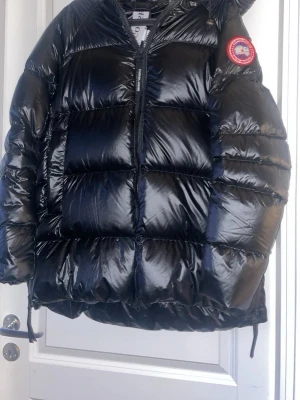 Svart pufferjacka från Canada Goose - Säljer en svart, glansig pufferjacka från Canada Goose med klassisk patch på ärmen. Aldrig använd med lapparna kvar. Pris kan diskuteras!!