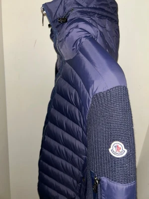 Blå dunjacka med stickade ärmar Moncler - Snygg blå dunjacka från Moncler. Moncler-logga på ärmen ger en exklusiv touch. Perfekt för våren. Det går även att scanna. 
