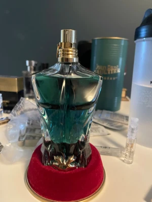 Jean Paul Gaultier Le Beau parfym - Jean Paul Gaultier Le Beau parfym i en unik flaska formad som en manlig torso. Flaskan är transparent med turkosblått innehåll och gulddetaljer. Kommer med original grön metalltub och röd sammetsbas. Perfekt för dig som gillar snygg design och fräscha dofter.