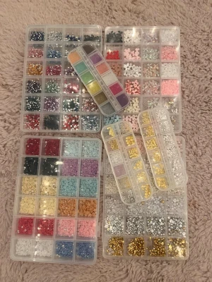 Stort kit med nageldekorationer - Säljer ett stort kit med nageldekorationer i olika färger och former. Innehåller strass, glitter, pärlor och små figurer i plast och metall. Perfekt för att skapa unika och kreativa nageldesigner. Kommer i praktiska förvaringsboxar med många fack.