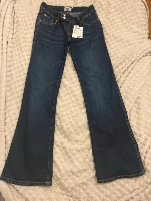 Blå bootcut jeans från lager 157 - Snygga blå bootcut jeans från lager 157 med klassisk femficksmodell och orangea kontrastsömmar. Jeansen har låg midja och utsvängda ben. Tillverkade i denim med en djupblå tvätt och detaljer i metall. Perfekta för en trendig och avslappnad stil.