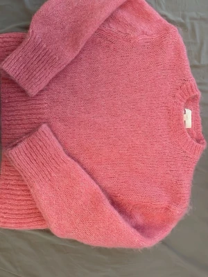 Rosa fluffig stickad tröja - Stickad tröja från H&M. Tröjan är i storlek XXS, och materialet består av både ULL och ALPACA. Tröjan är i ”nytt skick” då jag aldrig har använt den efter köpet, men då den inte kommer i original förpackning eller med prislapp på så kunde jag inte trycka in det.