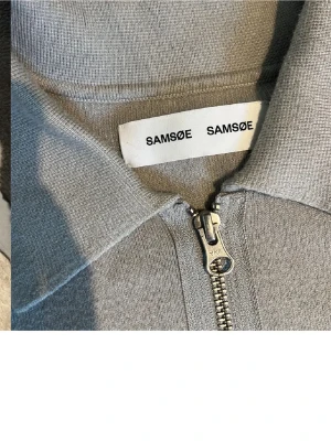 Ljusgrå ziptröja från Samsøe Samsøe - Snygg ljusgrå ziptröja från Samsøe Samsøe med krage och hel dragkedja framtill. Tröjan har en bröstficka och är tillverkad i mjukt stickat material. Perfekt för lager på lager och enkel att matcha med olika outfits. 