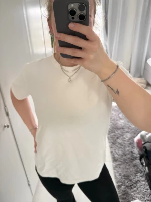 Vit basic t-shirt med rund hals - En enkel och stilren vit t-shirt med rund hals och korta ärmar. Perfekt för att matcha med jeans eller leggings. Materialet känns mjukt och bekvämt, och passformen är normal. Stickat material.