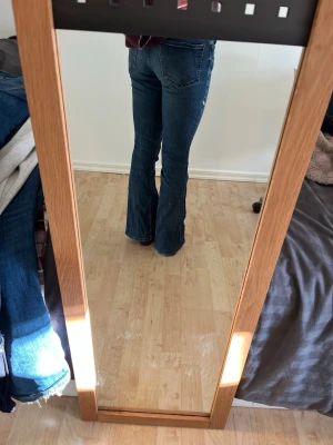 Blå bootcut jeans med medel midja - Säljer ett par klassiska blå bootcut jeans med medel midja och femficksmodell. Jeansen har en snygg tvätt och sitter tajt över låren för att sedan bli vidare nedtill. Perfekta till sneakers eller boots och ger en retrovibe till outfiten.