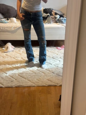Blå slitna raka jeans - Säljer ett par blå jeans med raka ben och slitningar på både lår och knän. 