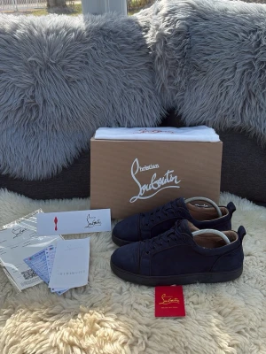 Mörkblå sneakers från Christian Louboutin - Snygga mörkblå sneakers från Christian Louboutin i mocka med matchande mörkblå sula och klassisk låg profil. Skorna har rund tå, ton-i-ton snörning och diskreta detaljer. Perfekta för dig som vill ha en clean och exklusiv look. Men ser på tredje bilden att de har blivit lite limmade men inget som syns eller märks. Låda, dustbag, kvitton, och Louboutin kort ingår. Tveka inte att fråga om ni har några frågor 😀