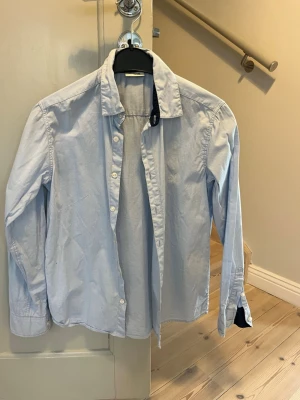 Ljusblå skjorta från Kappahl - Klassisk ljusblå skjorta från Kappahl med lång ärm och knappar framtill. Skjortan har en enkel, stilren design och är tillverkad i mjuk bomull.