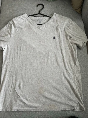 Grå t-shirt från Polo Ralph Lauren - Klassisk grå t-shirt från Polo Ralph Lauren med korta ärmar och rund hals. T-shirten har en liten mörkblå logga broderad på bröstet och är tillverkad i mjuk bomull. Perfekt basplagg för en avslappnad stil. Storlek L