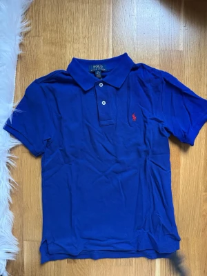 Blå pikétröja från Ralph Lauren - Aldrig använt. Storlek M (pojkar 10-12), passar som vuxen S/SX