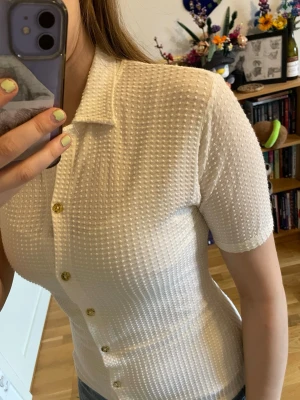 Vit kortärmad topp - Snygg vit topp med korta ärmar och knappar framtill. Blusen har en krage och ett strukturerat, prickigt tyg.  