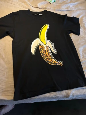 Svart t-shirt med banantryck - Cool svart t-shirt med ett stort tryck av en banan där skalet har leopardmönster. T-shirten har rund hals och korta ärmar. Perfekt för dig som vill sticka ut med en unik och lekfull design.