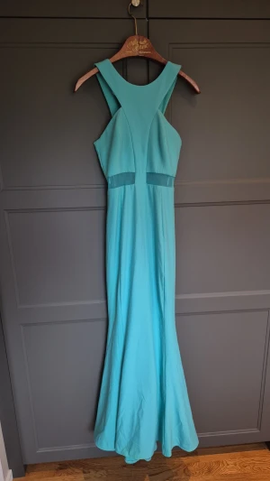 Turkos långklänning med meshdetalj - Snygg turkos långklänning med breda axelband och meshdetalj i midjan. Klänningen har en figurnära passform upptill och faller snyggt nedåt. Perfekt för dig som vill sticka ut med en färgstark look. Står stl 1 i klänningen så jag översätter det till 34/36 eller xs/s.