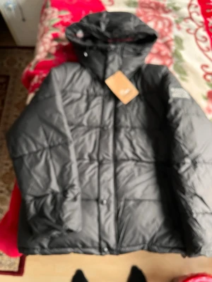 Svart pufferjacka från Burberry - Snygg svart pufferjacka från Burberry med huva och diskret logga på ärmen. Jackan har en quiltad design och stängs med knappar framtill. Perfekt för kalla dagar och riktigt trendig i vintergarderoben.