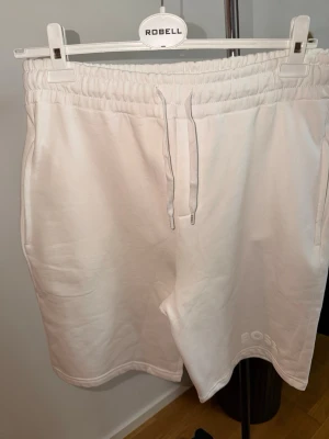 Vita shorts från BOSS med snörning - Snygga vita shorts från BOSS med broderad logga på benet. De har elastisk midja med snörning och är tillverkade i mjuk bomull, perfekta för en avslappnad stil. Klassisk passform och neutrala detaljer gör dem enkla att matcha.