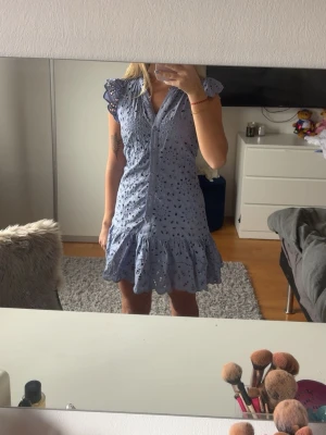 Ljusblå broderad kortklänning - Supersöt ljusblå kortklänning med volangkant och broderade detaljer. Klänningen har knappar framtill, v-ringning och korta ärmar med volang. Perfekt för sommarens alla tillfällen💕