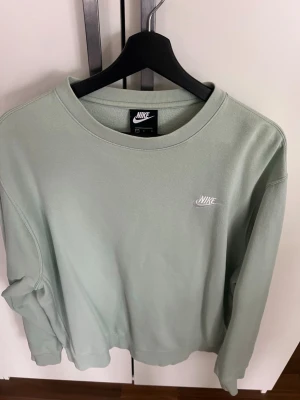 Ljusgrön sweatshirt från Nike - Snygg ljusgrön sweatshirt från Nike med klassisk rund halsringning och diskret Nike-logga broderad i vitt på bröstet. Tröjan har en avslappnad passform och är tillverkad i mjukt bomullsmaterial. Perfekt för en casual och sportig stil. Strl L