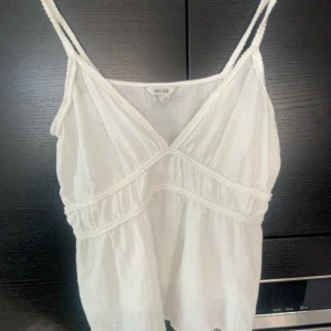 Vit linnetopp från Aware - Säljer en söt vit linnetopp från Aware med smala axelband och v-ringning. Toppen har dekorativa sömmar och en luftig, lätt passform som passar perfekt till sommaren.