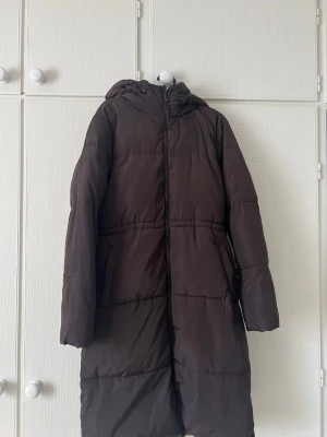Lång brun jacka med huva - Jacka från Cubus, säljer den då jag tycker att den inte värmer tillräckligt mycket. Fint skick men använd. Innerfodret inte helt perfekt då det krångla i tvätten. Köparen står för frakt!☺️