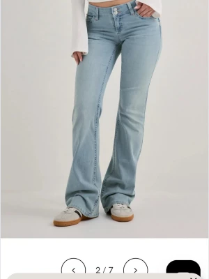 Ljusblå bootcut jeans med hög midja - Säljer ett par ljusblå bootcut jeans. Jeansen har en snygg utsvängd passform och är tillverkade i mjukt denimtyg. Perfekta för en trendig och avslappnad look. Dom har några hål längs ner eftersom att dom är ganska långa men inget som märks tydligt