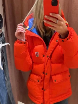 Röd dunjacka från Fjällräven - Snygg röd dunjacka från Fjällräven med blått innerfoder och gula detaljer på huvan. Modell EXPEDITION DOWN LITE JACKET W. Som ny knappt använd. Skriv om frågor eller fler bilder