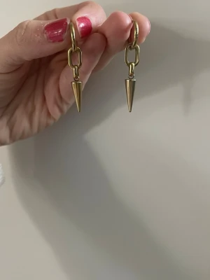 Guldtonade örhängen med konform - Säljer ett par trendiga örhängen i guldtonad metall med kedjedetalj och konformad hängande spets. 