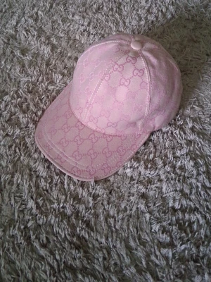 Rosa Gucci keps med GG-mönster - Säljer en snygg rosa keps från Gucci med det klassiska GG-monogrammet över hela kepsen. Kepsen har böjd skärm och är tillverkad i ett tygmaterial som ger en exklusiv känsla. Perfekt för dig som vill ha en trendig och lyxig accessoar. Pris man diskuteras.