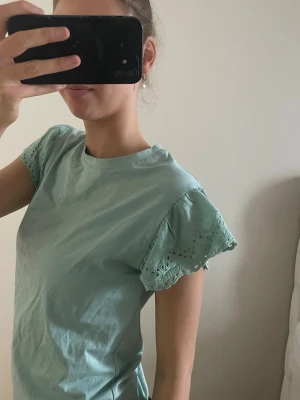 Ljusgrön topp med spetsärmar - Supersöt ljusgrön topp med korta ärmar i spetsdetalj. Toppen har en avslappnad passform och rund halsringning. Perfekt för dig som vill ha något enkelt men ändå med en twist. Materialet känns mjukt och skönt mot huden.