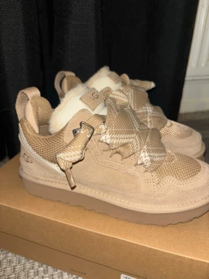 Beige sneakers från UGG med rutiga snören - Säljer ett par beige sneakers från UGG med rutiga snören i beige och vitt. Finns även vitt fluff i skorna. Skorna är i färgen sand och köpa från merch sweden för 34999 kr. Skorna är använda 1 gång samt har extra snören med.