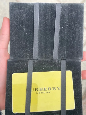 Burberry plånbok med rutigt mönster - Snygg plånbok från Burberry med klassiskt beige, svart och rött rutmönster. Insidan har svarta tygband för kort och fack för förvaring. Perfekt för dig som gillar stilrena accessoarer med ikonisk design.