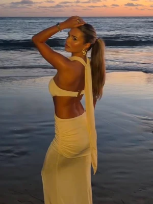 Vit långklänning med omlott och slits - Elegant vit långklänning med omlott-detaljer och slits. Klänningen har öppen rygg och halterneck med knytband som faller ner längs ryggen. Materialet ser ut att vara lätt och flödande, perfekt för sommarkvällar. Passformen är slim och klänningen har en modern, stilren look.