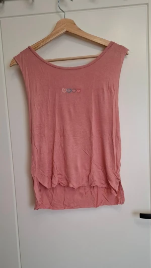 Rosa ärmlös topp från Pink Tree - Söt rosa ärmlös topp från Pink Tree med broderade hjärtan i olika färger framtill. Toppen har en lös passform och rund halsringning. Perfekt för varma dagar och enkel att matcha med jeans eller kjol.
