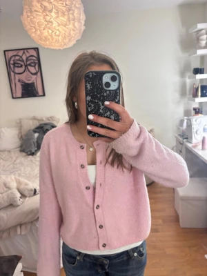 Ljusrosa kofta med knappar - Söt ljusrosa kofta med rund hals och knappar framtill. Koftan är stickad och har långa ärmar. Materialet är mjukt och skönt.