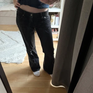 Svarta bootcut jeans med låg midja - Säljer ett par svarta bootcut jeans med låg midja och klassisk femficksmodell. Jeansen har en snygg passform som sitter tajt upptill och släpper ut vid benen. Perfekta för dig som gillar en retroinspirerad look.