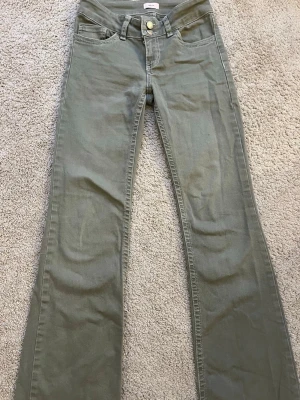 Olivgröna bootcut jeans från Nelly - Snygga olivgröna jeans från Nelly med bootcut-modell och klassisk femficksdesign. Jeansen har normal midja och stängs med knapp och dragkedja. Perfekta för dig som vill ha en avslappnad men trendig look.
