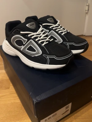 Dior B30 - Snygga svarta Dior sneakers med vita och grå detaljer samt tydlig CD-logga på sidan. Skorna har vit sula, vita skosnören och är tillverkade i mesh och syntetmaterial. Perfekta för dig som vill sticka ut med exklusiva och trendiga sneakers.      !!PRIS KAN SÄNKAS VID SNABB AFFÄR!!