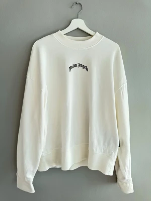 Vit sweatshirt från Palm Angels - Säljer en clean vit sweatshirt från Palm Angels med svart logotyptryck fram på bröstet och stort tryck på ryggen. Oversized fit med rund hals och ribbade muddar. Tillverkad i mjuk bomull för maximal komfort och streetwear-vibe. Använd 2 gånger köpt från end. I Milano 