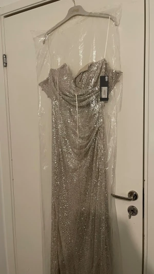 Glittrig långklänning med paljetter, förlovning  - Snygg axelbandslös långklänning i silver med glittriga paljetter över hela klänningen. Draperad upptill och figurnära passform som ger en elegant look. Perfekt för dig som vill sticka ut och glänsa på bal eller fest.
