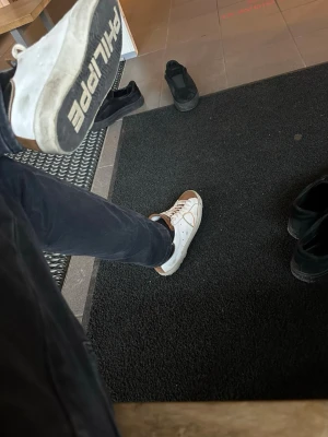 Vita PHILIPPE MODEL sneakers - Snygga vita sneakers från PHILIPPE MODEL med svarta och beige detaljer. Skorna har en klassisk låg siluett, vita snören och gummisula med tydlig logotyp undertill. Perfekta för dig som gillar att vara lite schysstare och vill ha något trendigt på fötterna.